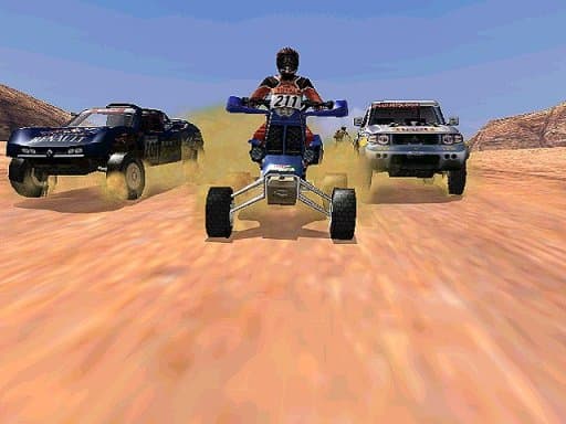 Quad rider facing the camera with two rally vehicles behind on a sandy track